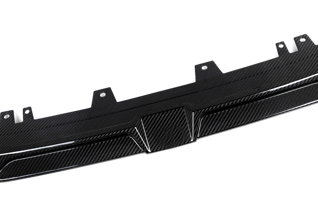 A carbon fiber car diffuser lies flat, showing textured pattern and mounting brackets, set against a plain white background.