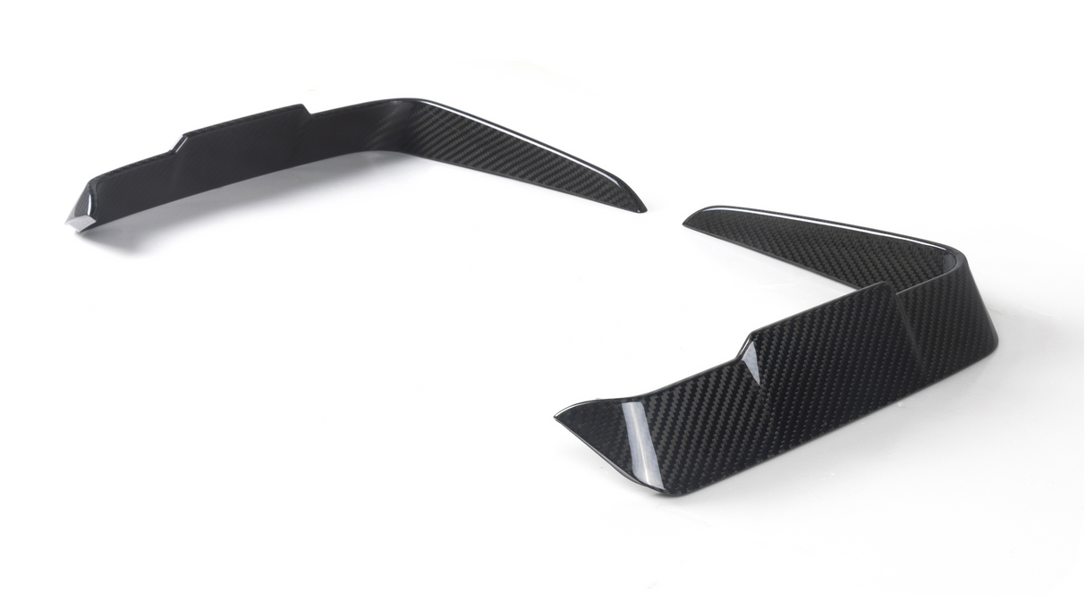 Two carbon-fiber vehicle splitters angled upward, placed on a white surface, likely designed for aerodynamics, showing a modern, sleek pattern.