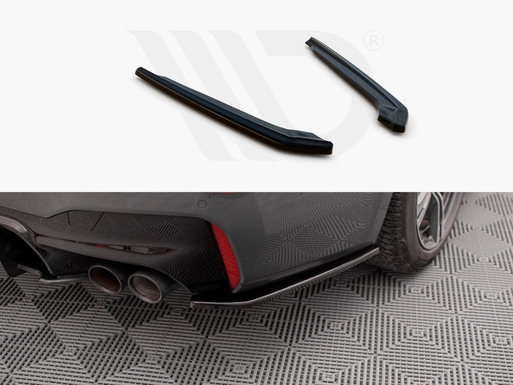 Two black car parts displayed above an installed piece on a car's rear bumper near dual exhaust pipes. The car is parked on a patterned surface.