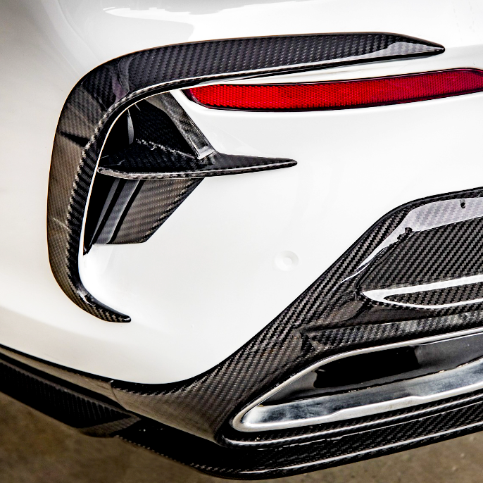 Carbon fiber car detail, featuring aerodynamic fins and trim around a tail light, situated on a white vehicle. The design contributes to a sporty, high-performance appearance.