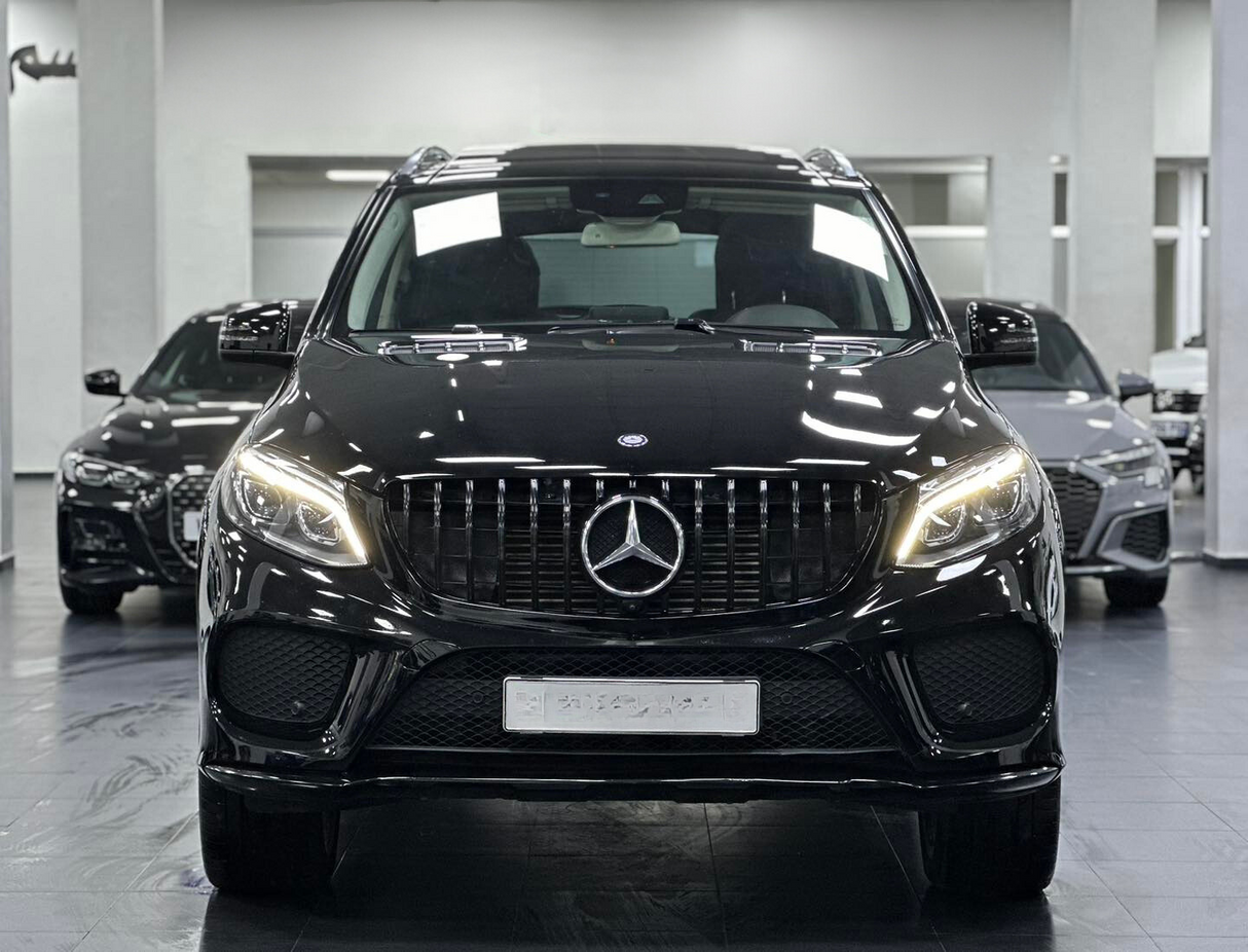 A black Mercedes-Benz SUV stands prominently with headlights on, inside a showroom, flanked by two other black cars in the background.