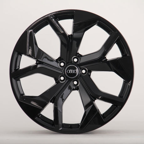 A glossy black alloy wheel with a five-spoke design featuring the Audi logo at the center, sits against a plain white background.