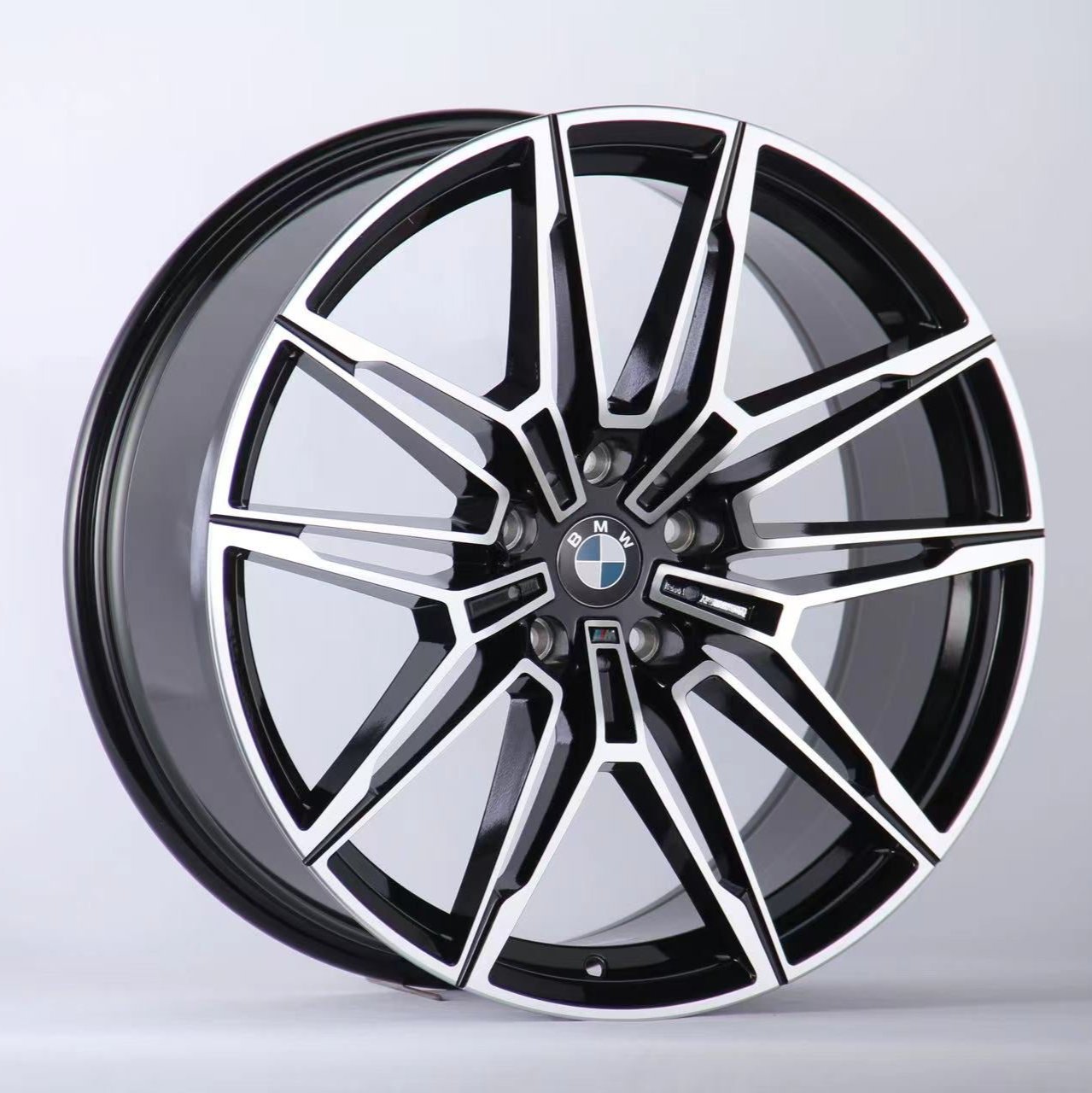 A black and silver multi-spoke alloy car wheel with a BMW logo is positioned upright against a plain white background, showcasing a sleek, modern design.