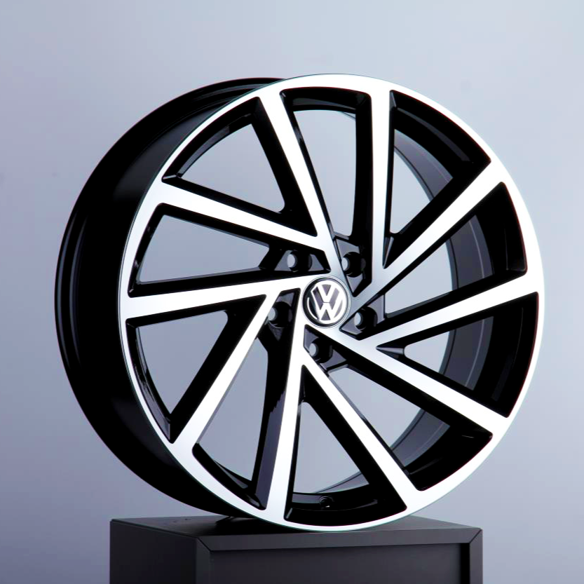 A stylish black and silver alloy wheel, featuring the Volkswagen logo, is displayed upright on a dark stand against a plain gray background.