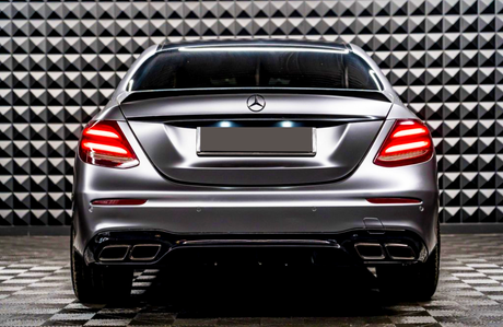 A sleek car with illuminated taillights is parked, facing a geometric-patterned wall in a showroom-like setting.