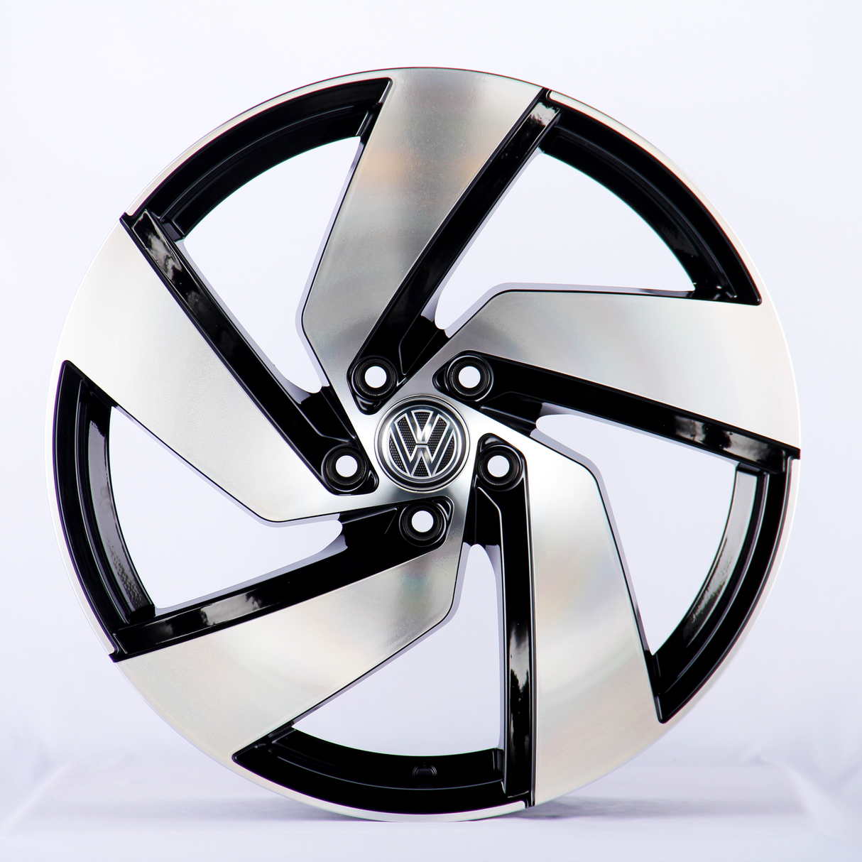 A five-spoke alloy wheel, featuring a polished black and silver design with a central logo, is positioned upright on a plain, light background.