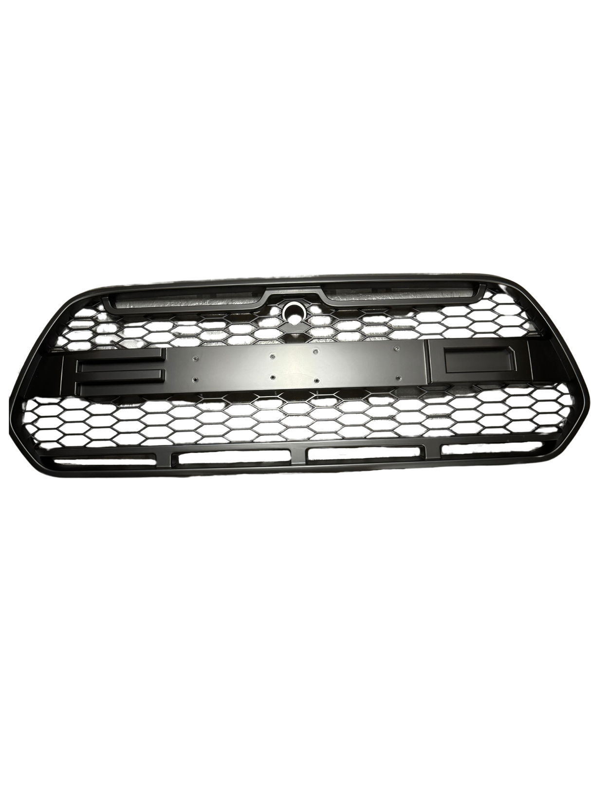 A black car grille with a hexagonal mesh pattern rests against a white background. The center features a circular cutout at the top part for a logo or emblem.