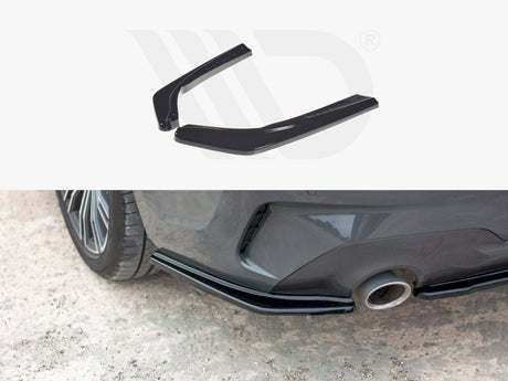 Two black car rear spoilers are displayed above an image showing them installed on a gray car's rear bumper next to the exhaust pipe, on a gravel surface.