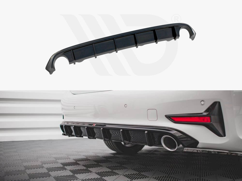 A curved black car diffuser with multiple fins sits in front of a parked white car, enhancing aerodynamics. The car is on a tiled floor within a garage-like setting.
