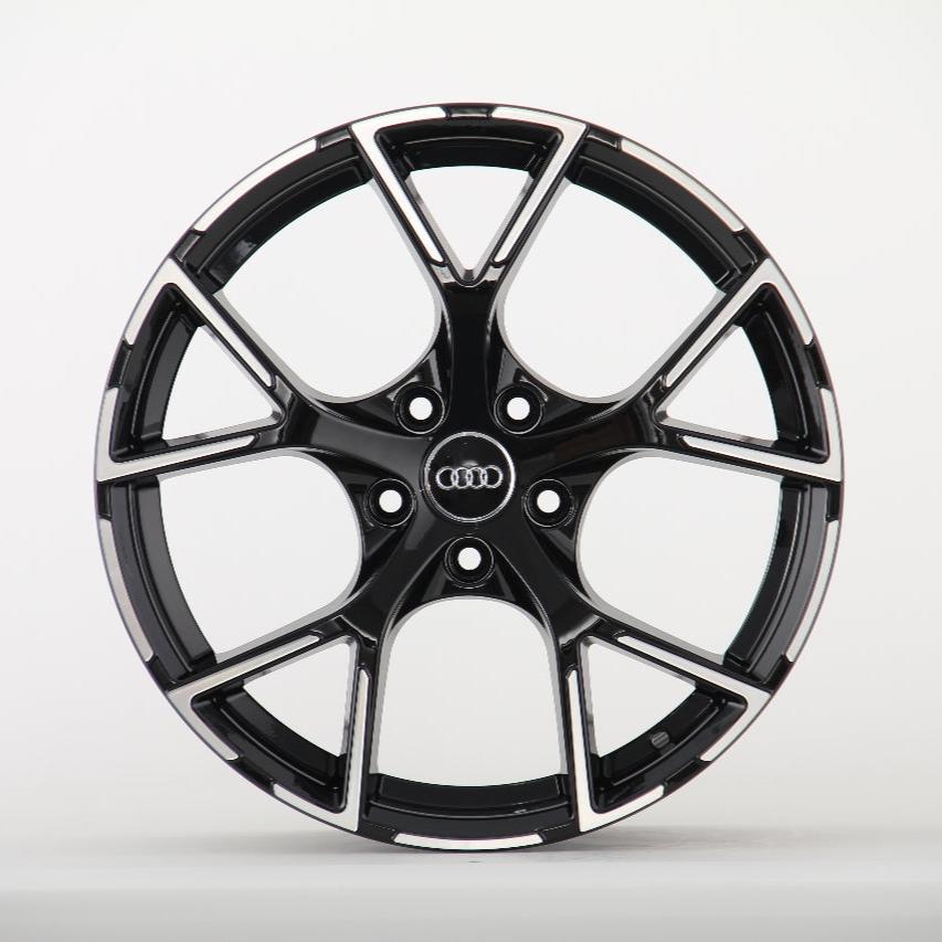 A glossy black and silver car wheel rim with five double spokes featuring the Audi logo at its center, set against a plain white background.