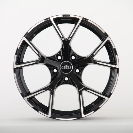 A glossy black and silver car wheel rim with five double spokes featuring the Audi logo at its center, set against a plain white background.