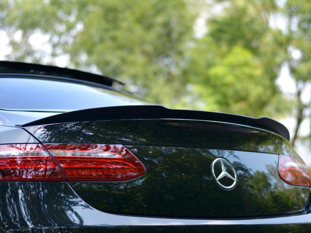 A black Mercedes-Benz car is parked outdoors, its rear showcasing a sleek spoiler and distinctive taillights. The green background of trees suggests a serene, natural setting.