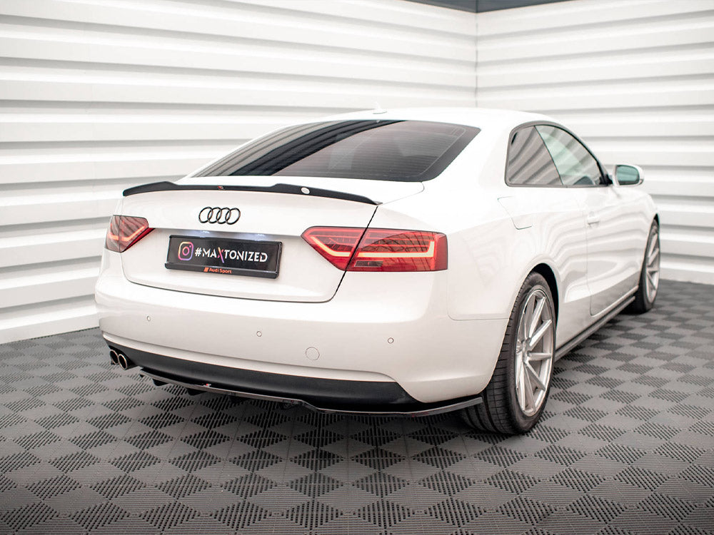 A white car is parked in a corner of a room with patterned flooring. The license plate reads "#MAATONIZED." The car is an Audi, surrounded by white, textured walls.