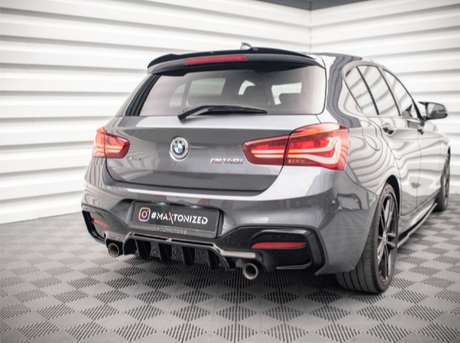 A gray BMW hatchback is parked on a patterned floor in a well-lit, corner room with white walls. The car features dual exhausts and red taillights. Text: "#MAXTONIZED".