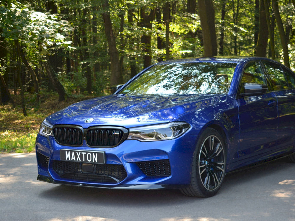 A blue car with sleek design stands parked on a shaded road, surrounded by dense green forest. The license plate reads "MAXTON."