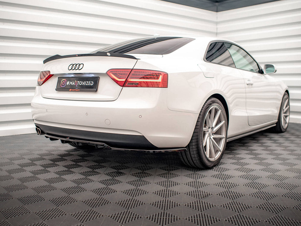 A white Audi coupe is parked, viewed from the rear in a stylish, modern garage with patterned flooring. The license plate reads "#MAXTONIZED" and features the Audi Sport logo.