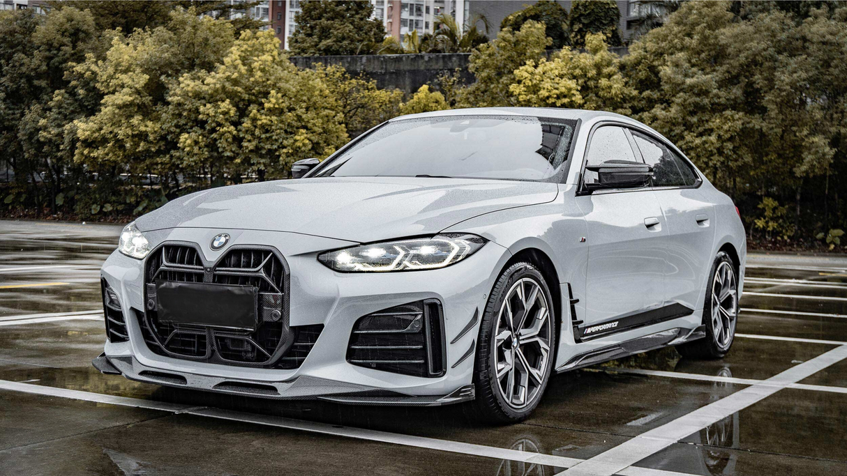 Car parked in a wet parking lot; it's a sleek, white sedan with distinctive headlights and sporty design details. Trees and buildings are visible in the background.