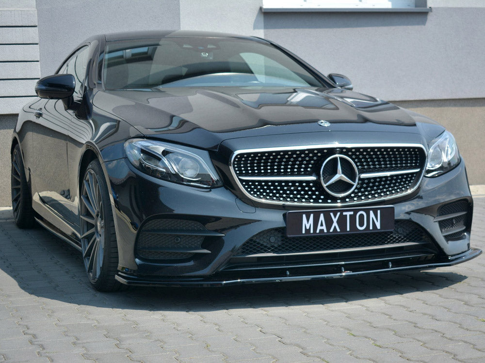 A black Mercedes-Benz car is parked on a paved surface, featuring a prominent grille with a star emblem. The license plate reads "MAXTON," and it's beside a modern building.