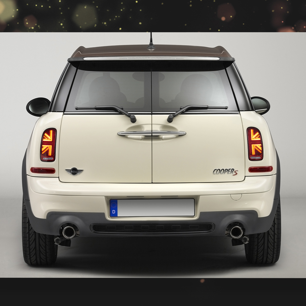 A cream-colored car, viewed from the rear, displays distinctive taillights and dual exhausts against a plain backdrop. The "Cooper S" badge and Mini emblem are visible.