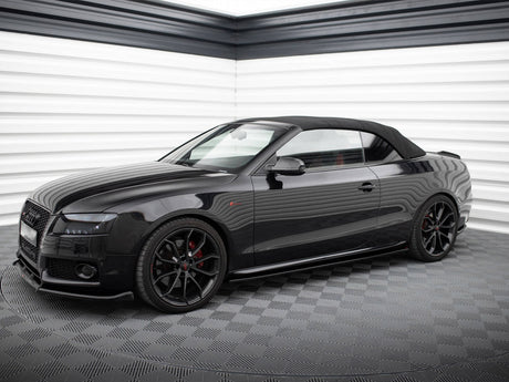 A sleek black convertible car with a soft top is parked in a modern, brightly lit, white-paneled showroom with a checkered floor.