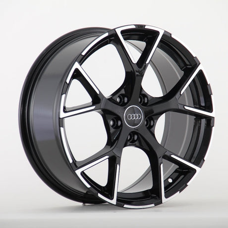 A black and silver alloy wheel with a five-spoke design, prominently featuring the Audi logo in the center, is displayed against a plain white background.