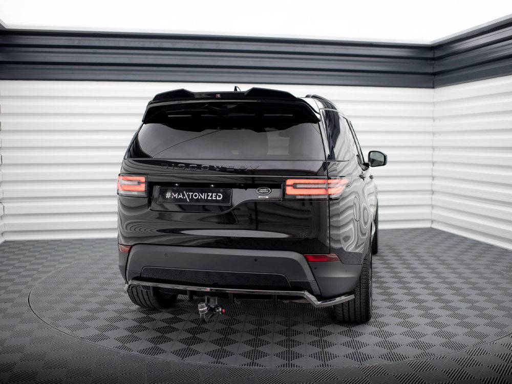 A black SUV is parked in a well-lit, indoor area with patterned flooring. The vehicle's license plate displays "#MAXTONIZED," and its rear lights are illuminated.