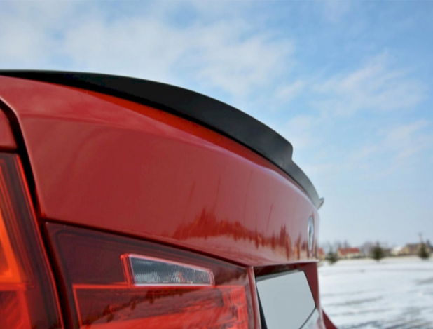 Red car trunk with a small spoiler. The car is stationary on a snow-covered field. The sky is clear with scattered clouds.
