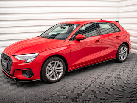 A red hatchback car is parked on a checkered-patterned floor, in a room with white, horizontally ribbed walls. The car features sleek lines and modern design elements.