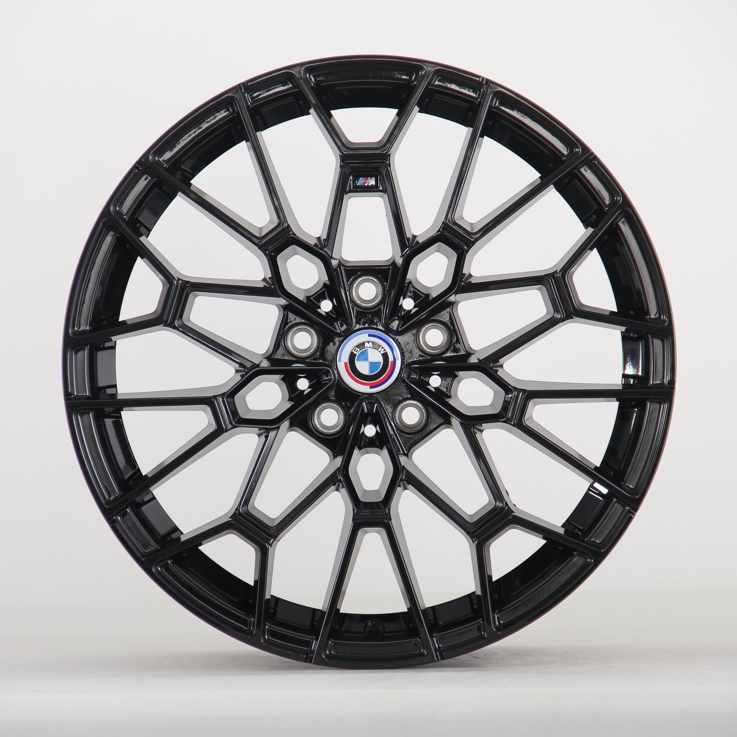 The image shows a black alloy wheel with a complex geometric design, featuring a blue, white, and red BMW logo at the center. The wheel is set against a plain white background.