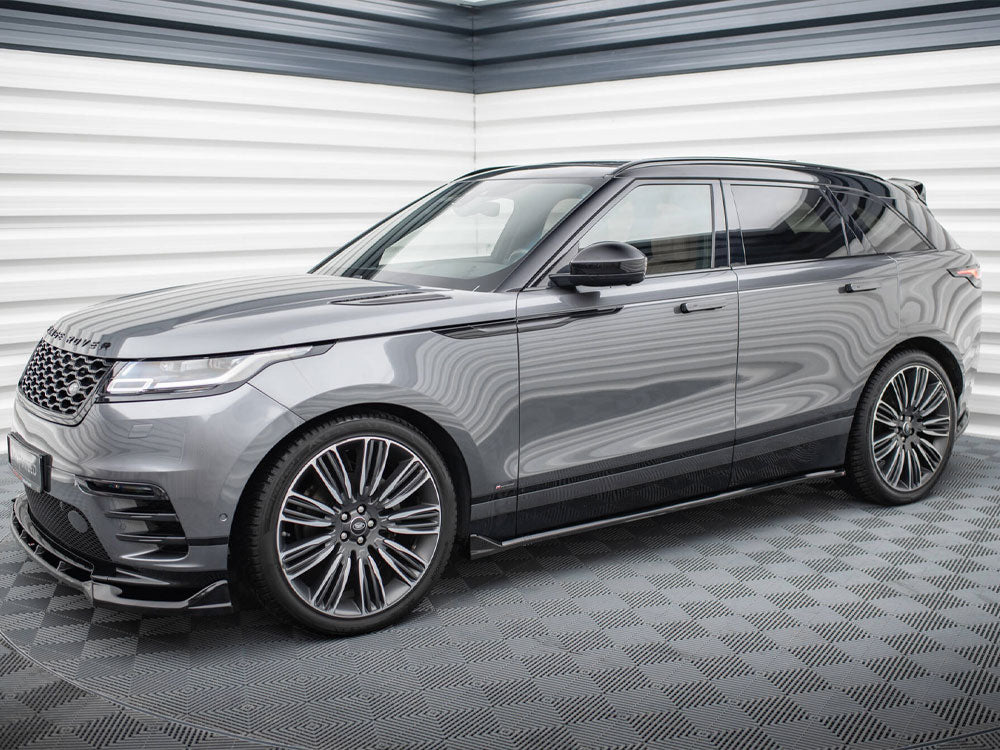 A sleek gray SUV is parked in a modern showroom with textured walls. It's a Range Rover, featuring large alloy wheels and a stylish, streamlined design.
