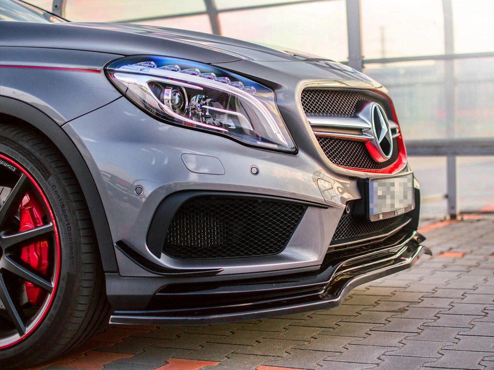 A silver car's front view parked on a tiled surface, featuring a prominent star emblem on the grille, sleek headlights, and red accents on the wheels, with glass panels in the background.