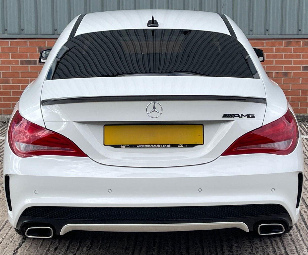 A white Mercedes-Benz AMG car is parked, featuring dual exhausts and tinted windows, against a backdrop of red brick and corrugated metal. Text: "www.mdscarsales.co.uk".
