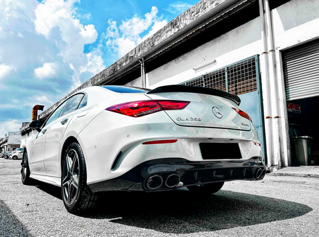 A white Mercedes-Benz CLA 250 faces away on a sunny day in an industrial area, parked near a building with a partially open garage door.