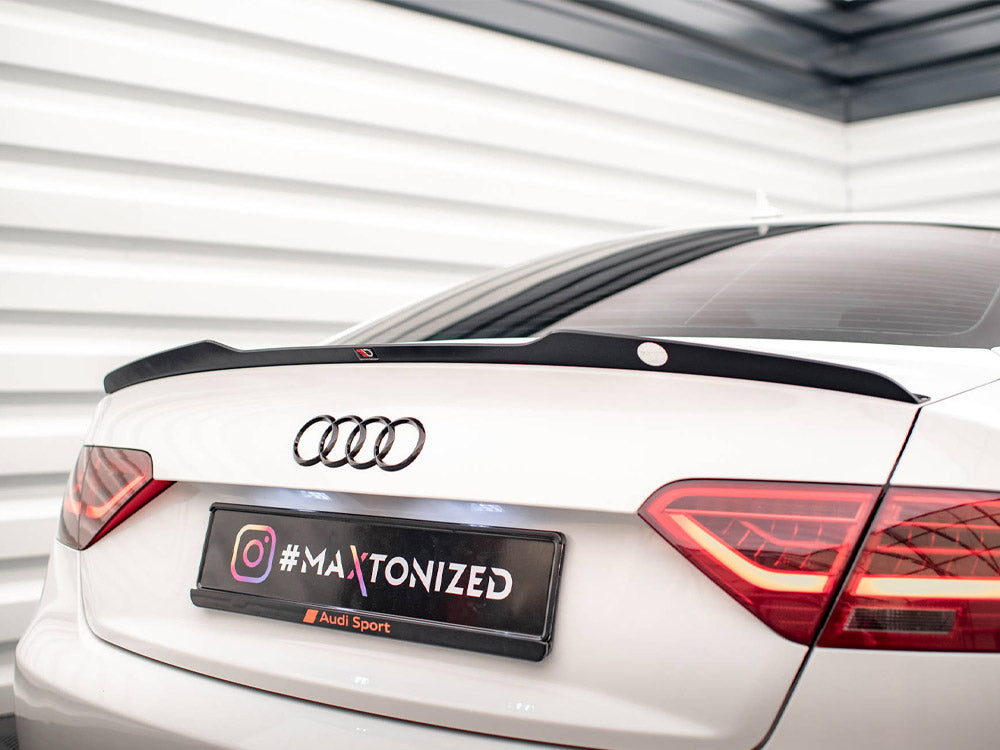 A white Audi car with a spoiler is parked in a corner with white geometric walls. The license plate reads "#MAXTONIZED" with an Instagram logo and "Audi Sport" below.