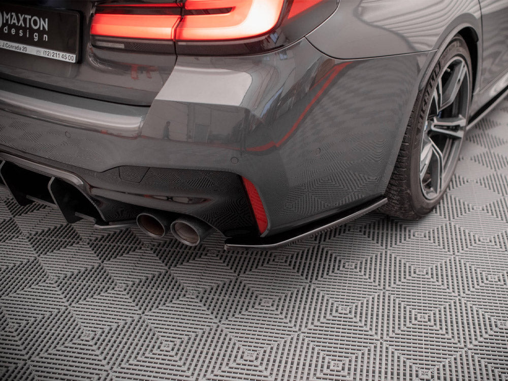 The rear of a grey car features illuminated taillights and dual exhaust pipes, stationary on a patterned floor. Visible text: "MAXTON design, J. Conrada 20, (12) 211 45 00."