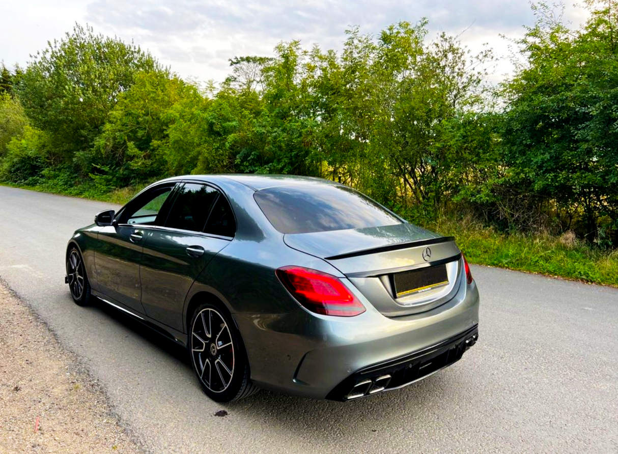 A gray sedan is parked on a quiet road, surrounded by lush green trees and bushes.