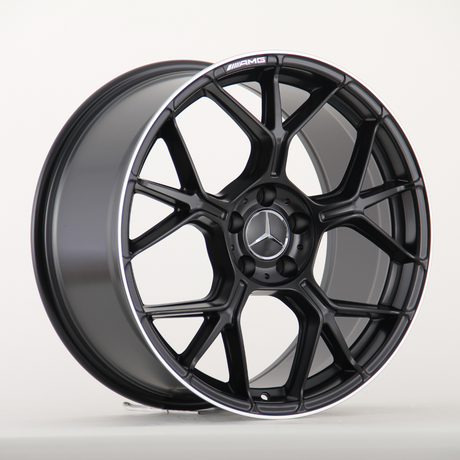 A black alloy car wheel features a multi-spoke design with the Mercedes-Benz emblem in the center. The AMG logo is written on the rim. It sits on a light surface.