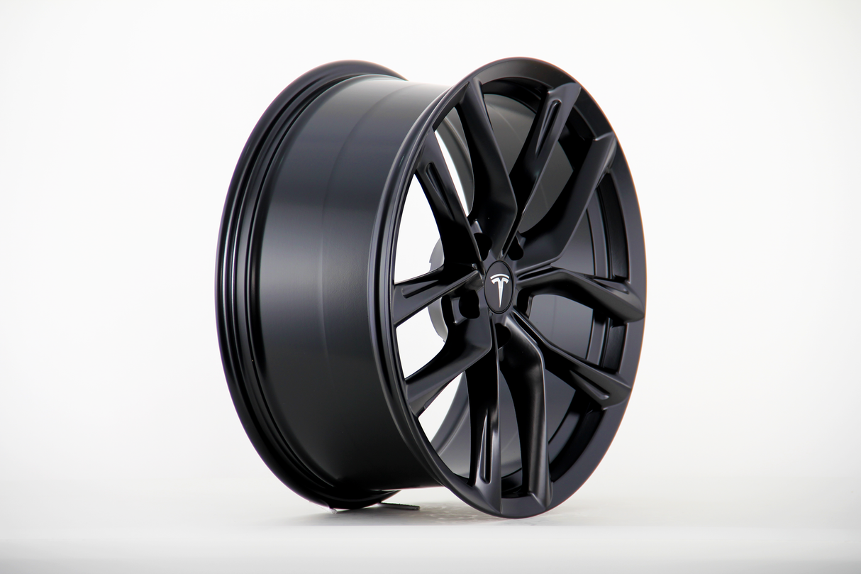 A black alloy wheel with a sleek, multi-spoke design displays a central logo resembling a "T," placed upright against a white background.