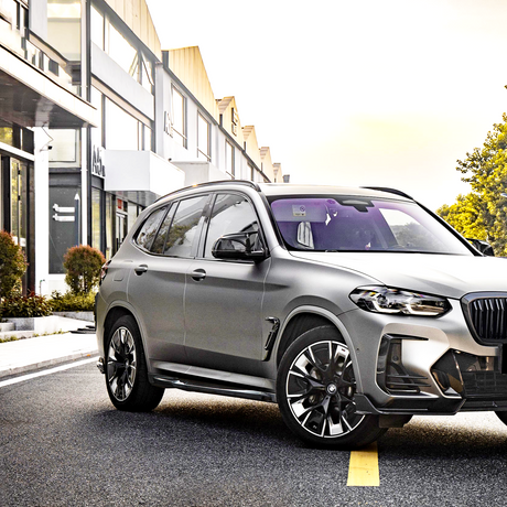 A silver SUV is parked on a city street, surrounded by modern buildings and greenery in an urban setting, with sunlight illuminating the scene.