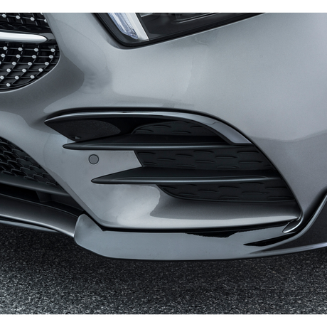 The front bumper of a sleek car features aerodynamic fins and grille details, highlighting its modern design, on a rough asphalt background.