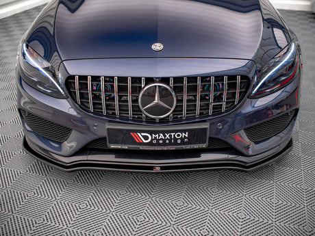 A dark blue car with a prominent front grille displaying a circular emblem sits on a textured floor. The license plate reads "MAXTON design" with contact information and AMG branding.