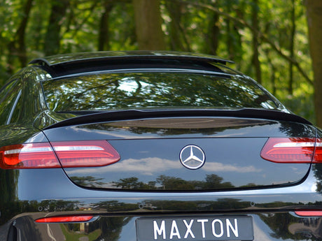 The black car is parked with a slightly open sunroof, displaying a Mercedes emblem and a license plate reading "MAXTON," surrounded by a lush forest environment.
