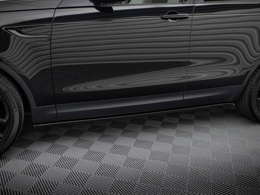 A black SUV side view shows reflections on its surface with "DISCOVERY" text near the front door. It stands parked on a textured gray floor, showcasing two tires.