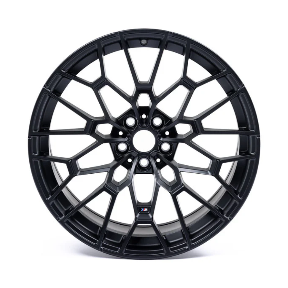 A black alloy wheel with a complex mesh design sits against a white background. The center features a small logo with blue and red stripes.
