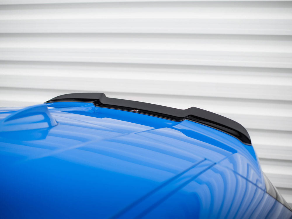 A blue car roof features a black spoiler. Set against a corrugated white background, the reflective surface of the car adds dynamic lines to the composition.