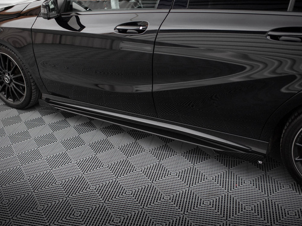 A sleek black car is parked on a geometric-patterned, gray floor. The car has tinted windows and black alloy wheels, reflecting a striped ceiling above.