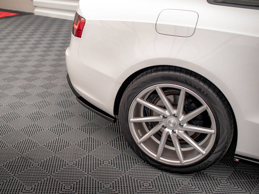Car rear wheel is parked on a textured gray garage floor. The white vehicle's body features a visible fuel cap, with red taillight on display in the upper corner.