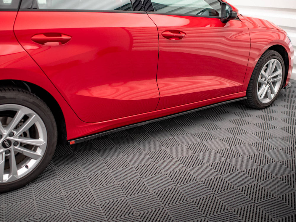A red car with two doors and silver wheels is parked on a patterned gray floor inside a well-lit room, reflecting the structured light above.