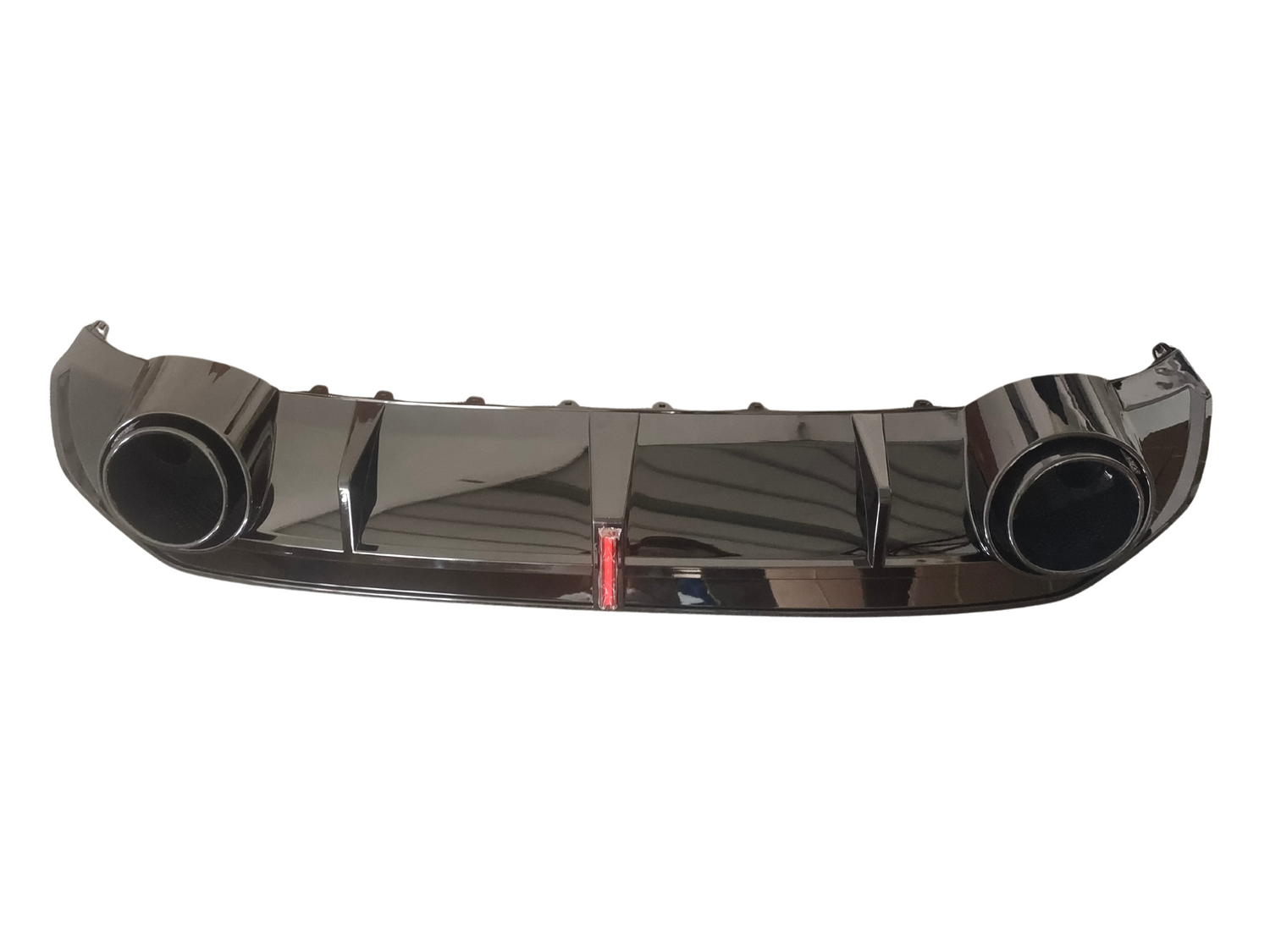 Shiny black car bumper features large circular exhaust openings on each side, with a red reflector in the center. It rests against a plain white background.