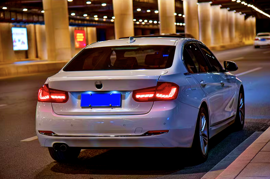 White car with illuminated taillights, parked in a well-lit tunnel, surrounded by other vehicles and glowing advertisements on nearby walls.